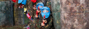 Group of boys and girls paintball players aiming and shooting with marker guns at opposing team outdoors
