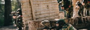 Paintball players crouching and prone beside a protective shelter made of wood