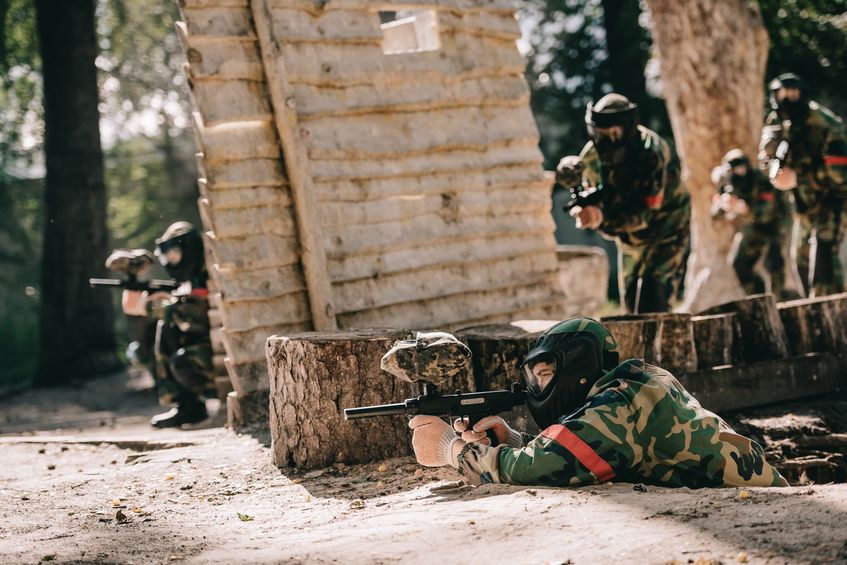 Paintball players crouching and prone beside a protective shelter made of wood